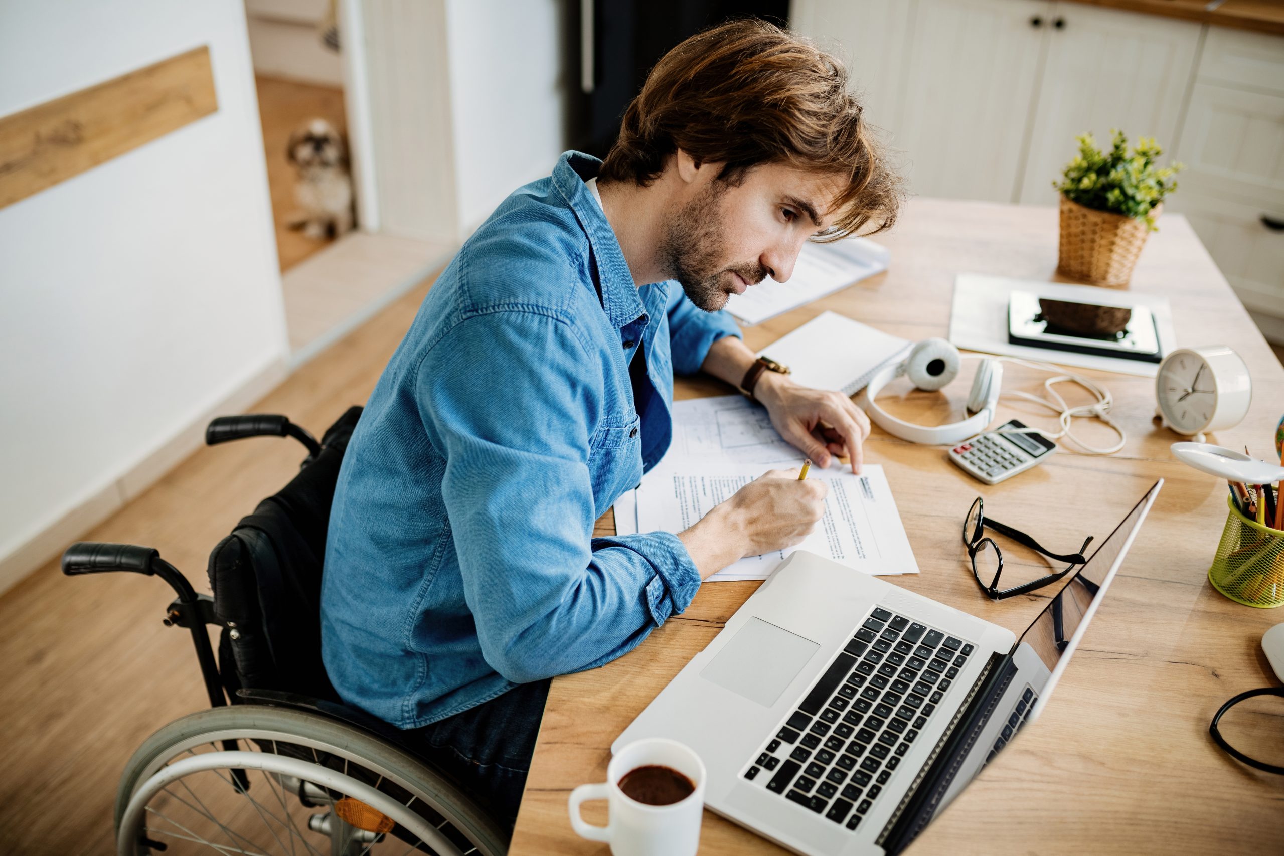 above-view-of-disabled-entrepreneur-writing-reports-while-using-laptop-at-home