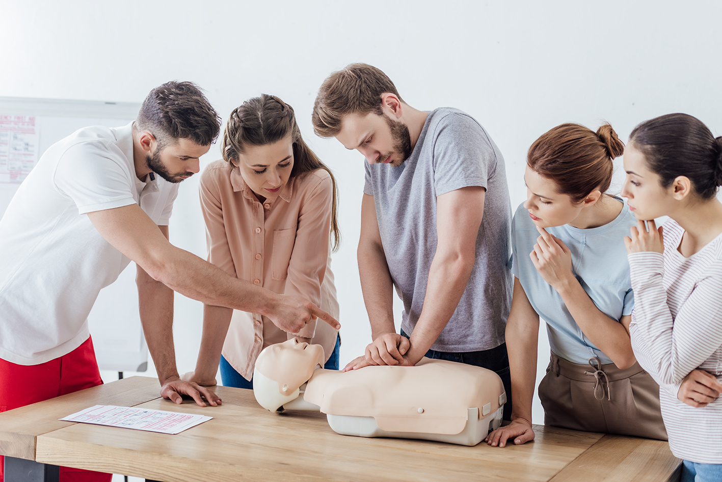 group-of-people-with-instructor-performing-cpr-on-dummy-during-first-aid-training