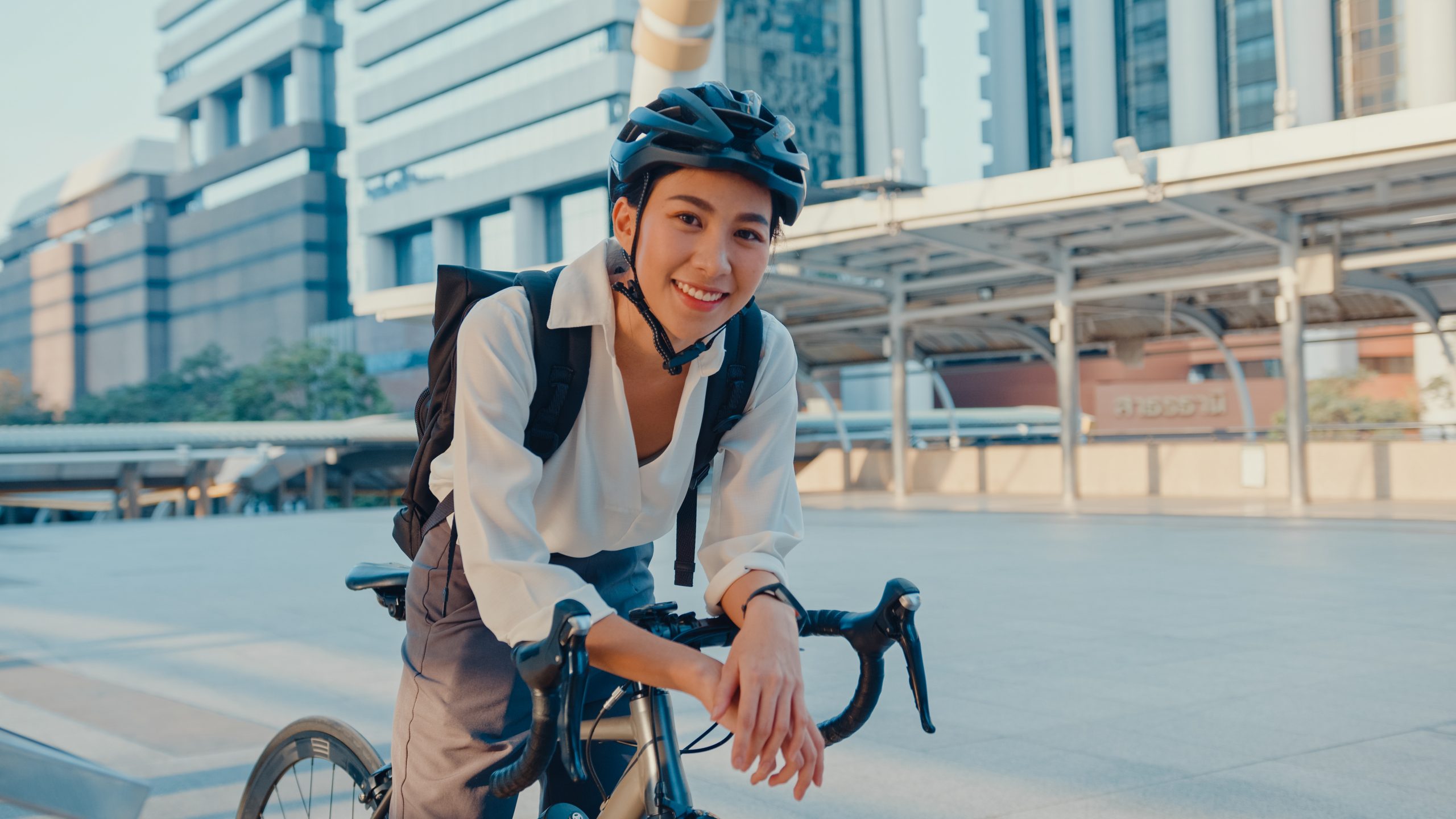asian-businesswoman-go-to-work-at-office-stand-and-smiling-wear-backpack-look-at-camera-with-bicycle-on-street-around-building-on-a-city-bike-commuting-commute-on-bike-business-commuter-concept